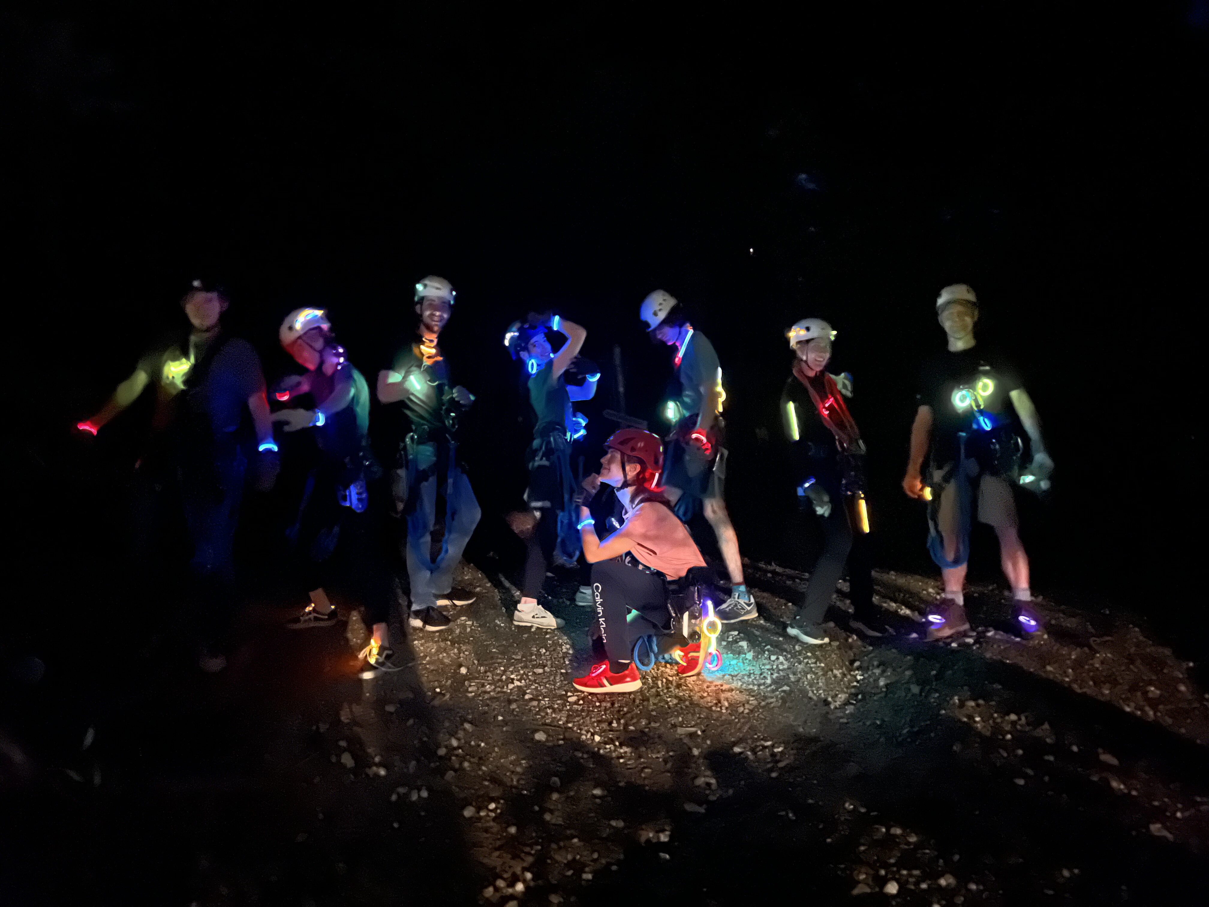 A group in helmets and harnesses on the mountain at night, lit up by glow bands and necklaces