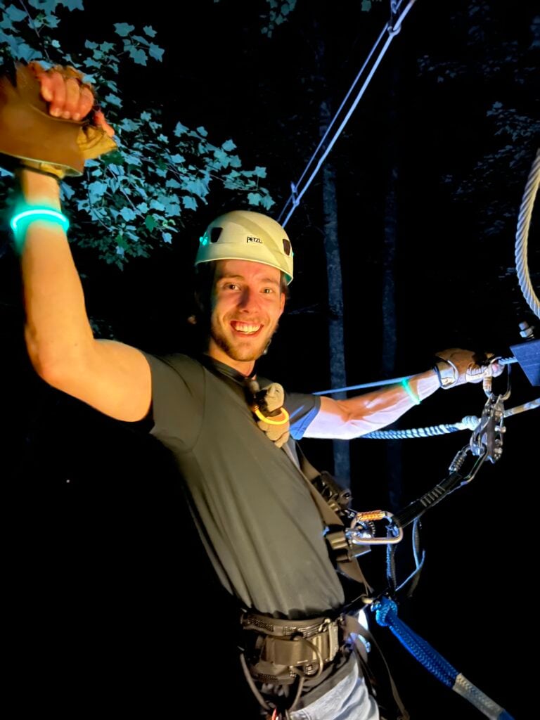 A smiling guest on the zipline at night, waving with a glow band on his wrist