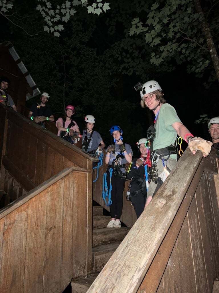 A smiling guest leads a group of riders up the wooden stairs at night