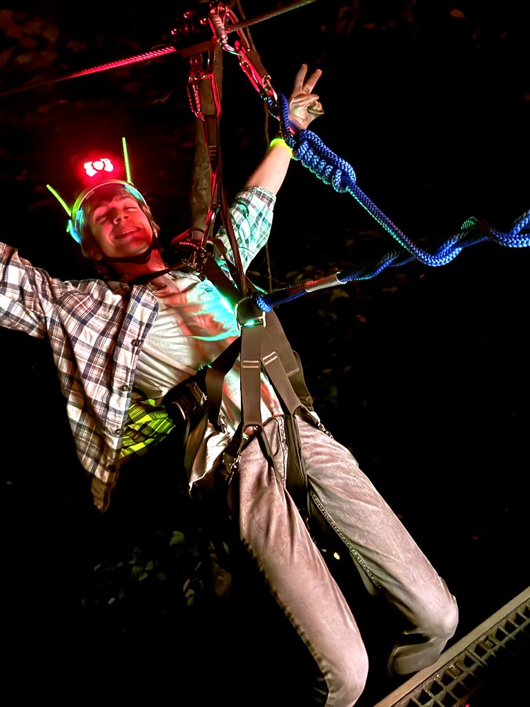 A rider with arms spread wide on a zipline at night
